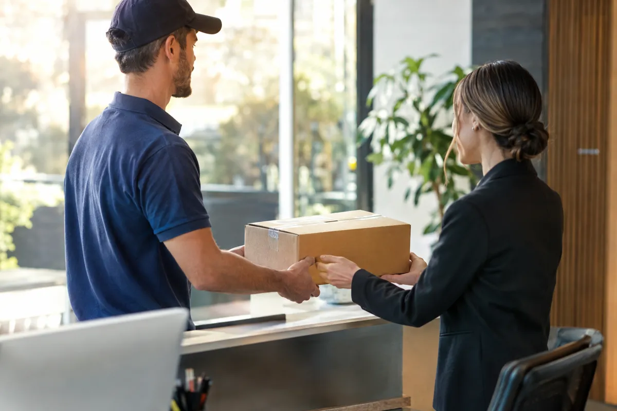 Delivery driver handing a package to a receptionist at an office front desk